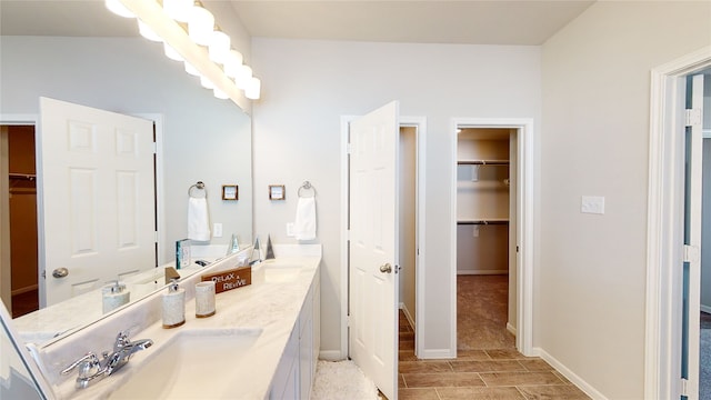 full bathroom featuring double vanity, a walk in closet, baseboards, and a sink