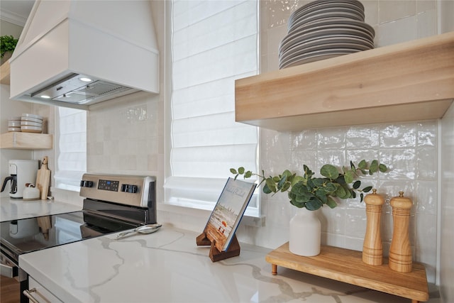 kitchen featuring electric range, tasteful backsplash, white cabinets, light stone countertops, and custom exhaust hood