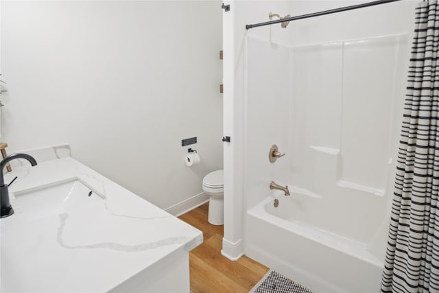 bathroom with toilet, shower / tub combo with curtain, a sink, wood finished floors, and baseboards