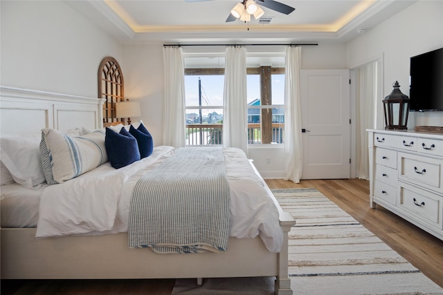 bedroom featuring a tray ceiling, wood finished floors, visible vents, and ceiling fan