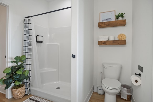 full bathroom with baseboards, wood finished floors, toilet, and a stall shower