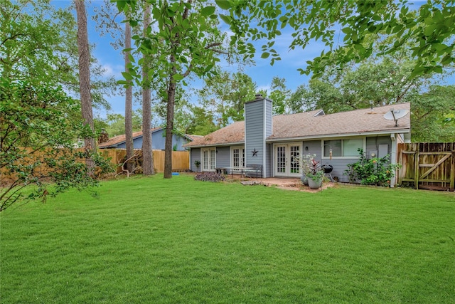 rear view of property featuring french doors, a lawn, a fenced backyard, and a chimney