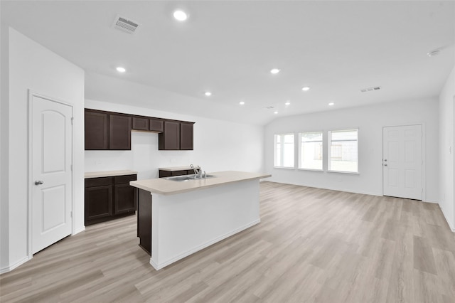 kitchen with visible vents, dark brown cabinetry, a center island with sink, light wood-type flooring, and a sink