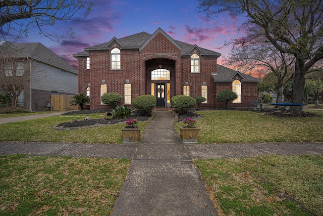 view of front of property with brick siding, a shingled roof, a front yard, and fence