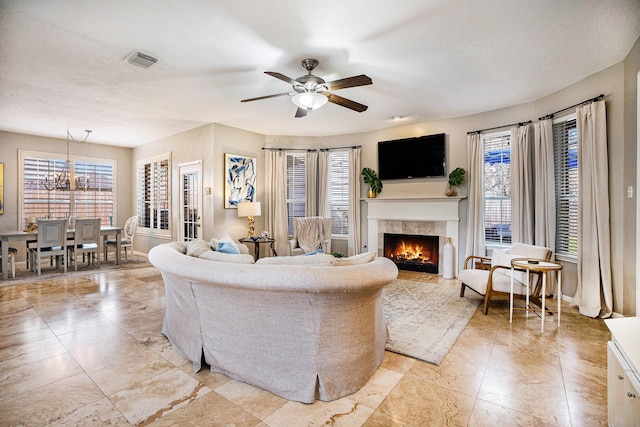 living area featuring plenty of natural light, ceiling fan with notable chandelier, visible vents, and a warm lit fireplace