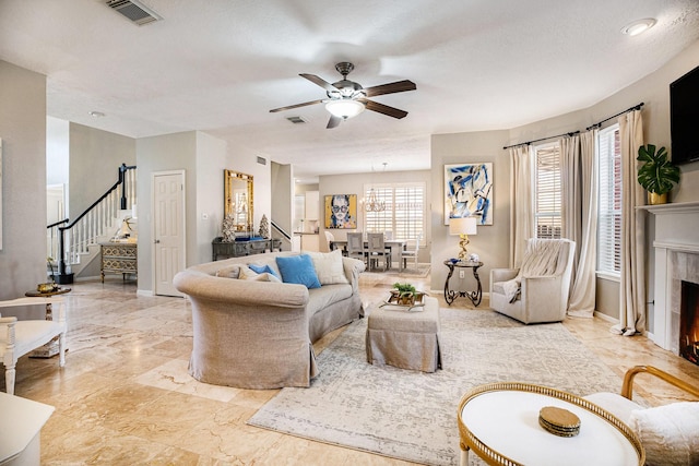 living room with a tiled fireplace, visible vents, stairs, and ceiling fan