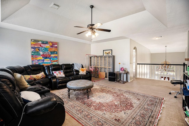 carpeted living room with a tray ceiling, arched walkways, visible vents, and ceiling fan