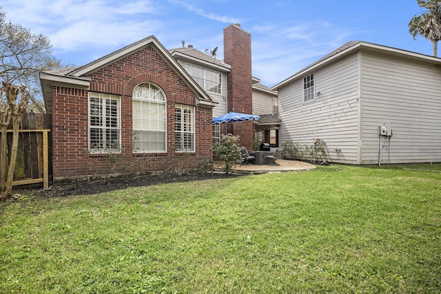 back of house featuring brick siding, fence, a chimney, a yard, and a patio