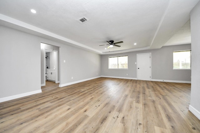 unfurnished living room with baseboards, visible vents, light wood finished floors, ceiling fan, and a raised ceiling