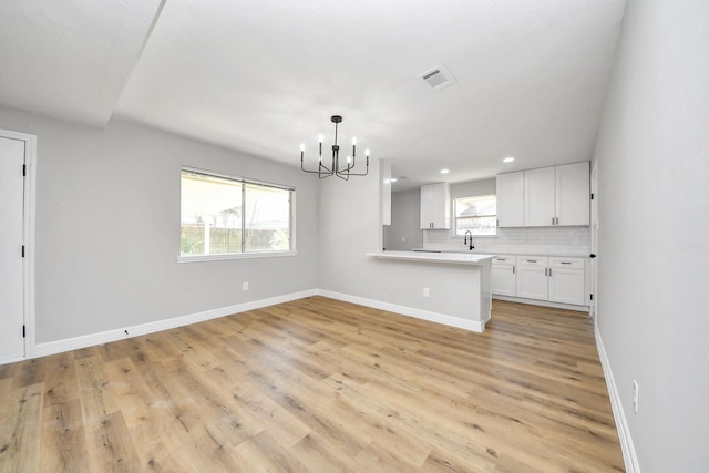 kitchen featuring baseboards, visible vents, white cabinets, a notable chandelier, and backsplash