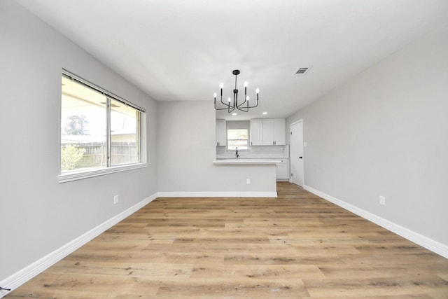 unfurnished dining area with a chandelier, light wood-style floors, and baseboards