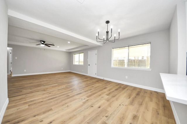 interior space featuring baseboards, a raised ceiling, ceiling fan with notable chandelier, and light wood finished floors