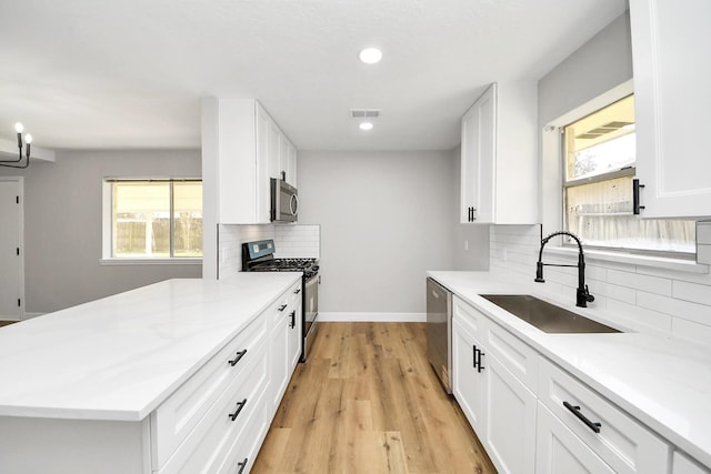 kitchen featuring light wood-style flooring, a sink, stainless steel appliances, white cabinets, and baseboards