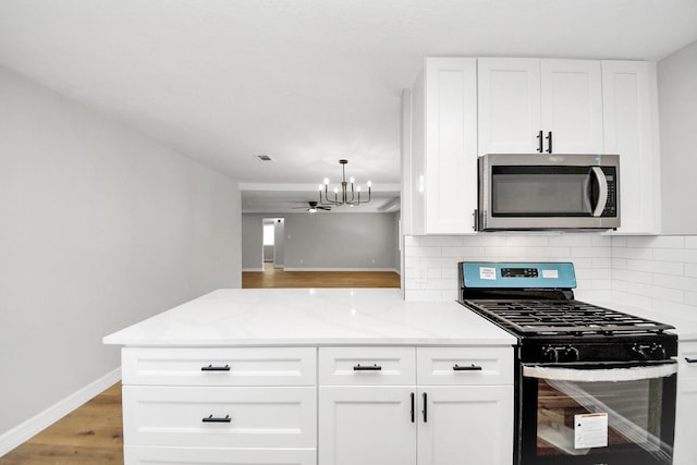 kitchen with stainless steel microwave, tasteful backsplash, white cabinets, gas range, and a chandelier