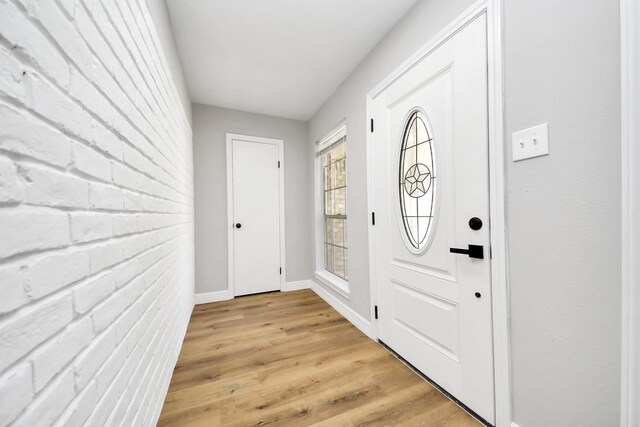 foyer with baseboards, light wood-type flooring, and brick wall