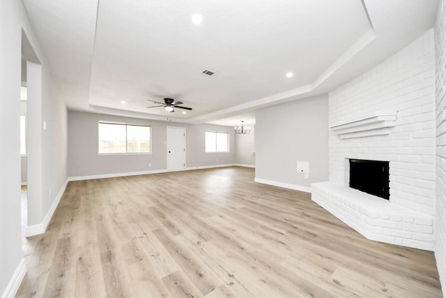 unfurnished living room with light wood-style flooring, visible vents, ceiling fan with notable chandelier, and a raised ceiling