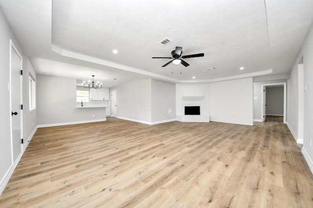 unfurnished living room featuring visible vents, baseboards, light wood-style flooring, a fireplace, and ceiling fan with notable chandelier