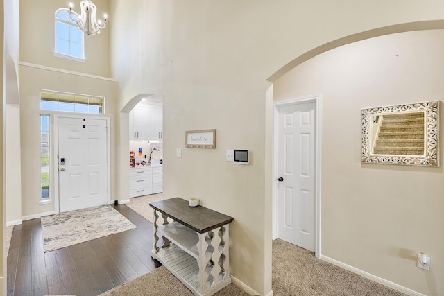 entrance foyer featuring arched walkways, an inviting chandelier, baseboards, a towering ceiling, and dark wood-style flooring