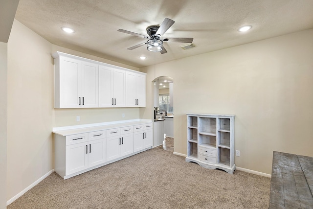 interior space with visible vents, light carpet, a ceiling fan, arched walkways, and baseboards