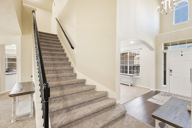 foyer with a chandelier, stairs, a towering ceiling, wood finished floors, and arched walkways