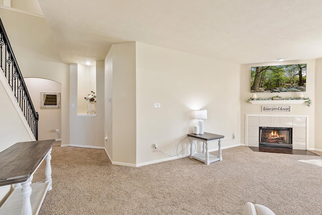 unfurnished living room with carpet, baseboards, a fireplace, arched walkways, and stairs