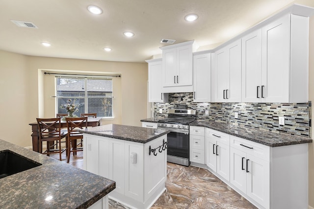 kitchen featuring decorative backsplash, stainless steel range with gas stovetop, visible vents, and a kitchen island