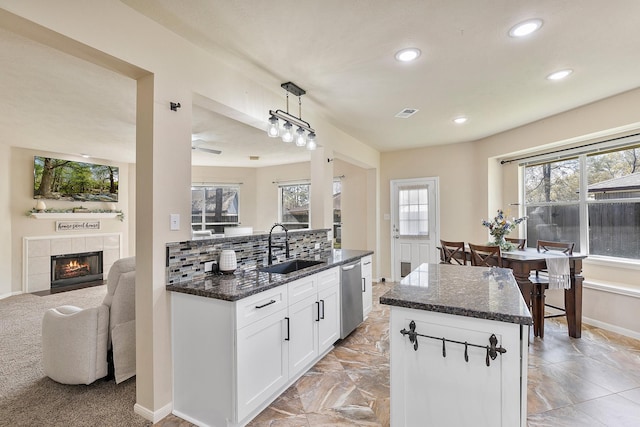 kitchen featuring a sink, a tiled fireplace, dark stone countertops, white cabinetry, and stainless steel dishwasher