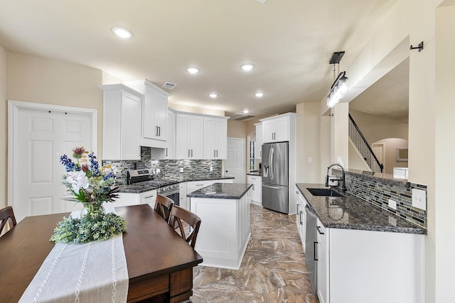 kitchen with dark stone countertops, arched walkways, a sink, appliances with stainless steel finishes, and marble finish floor