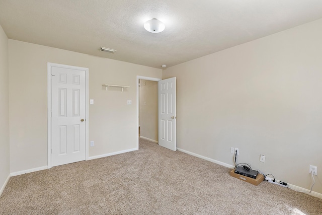 spare room with a textured ceiling, carpet, visible vents, and baseboards