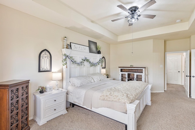 bedroom featuring a tray ceiling, light carpet, baseboards, and ceiling fan