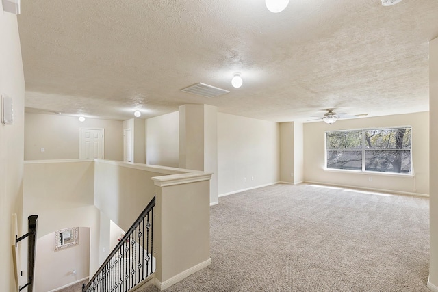 hallway with visible vents, carpet floors, baseboards, a textured ceiling, and an upstairs landing