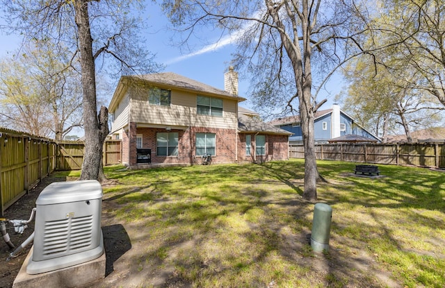 rear view of property with brick siding, a fire pit, a lawn, a chimney, and a fenced backyard