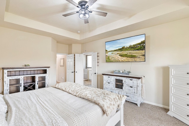 bedroom featuring baseboards, a raised ceiling, light colored carpet, and ceiling fan