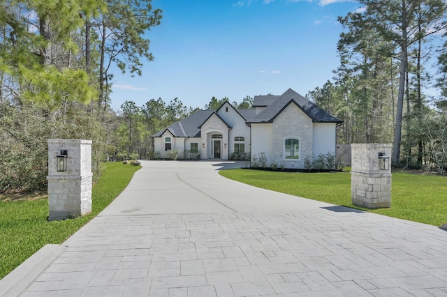 french country home with a front lawn, stone siding, and driveway