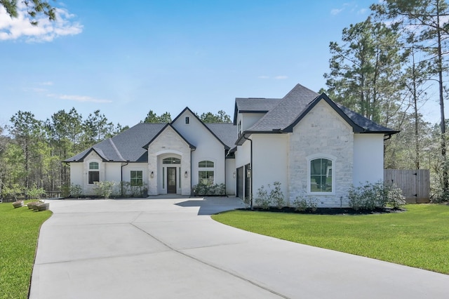 french country inspired facade featuring a front lawn, stucco siding, a garage, stone siding, and driveway