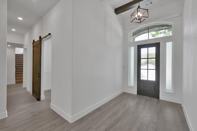 foyer featuring visible vents, baseboards, light wood-style floors, a barn door, and a notable chandelier