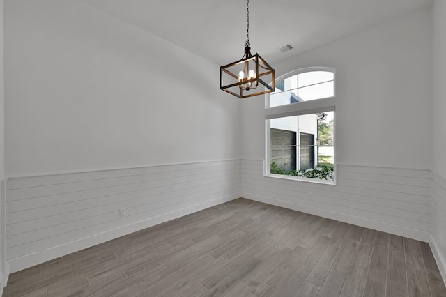 unfurnished dining area featuring a chandelier, a wainscoted wall, visible vents, and wood finished floors