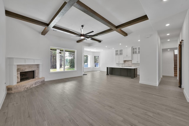 unfurnished living room featuring a stone fireplace, baseboards, light wood-type flooring, and ceiling fan