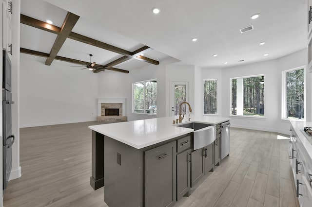 kitchen featuring a ceiling fan, light wood-style flooring, a kitchen island with sink, a sink, and stainless steel dishwasher