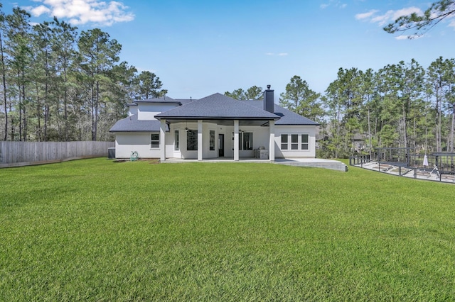 rear view of property featuring fence, roof with shingles, a lawn, a chimney, and a patio area