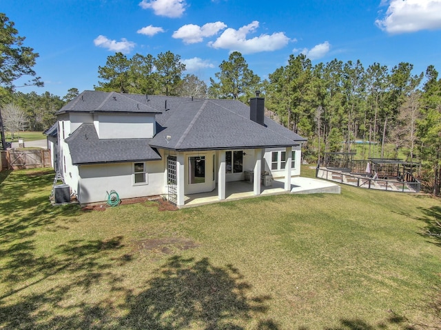 rear view of property with stucco siding, a lawn, a shingled roof, a chimney, and a patio area