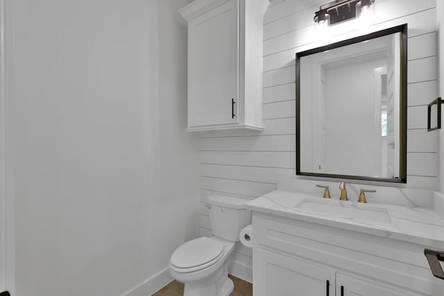 bathroom with vanity, toilet, baseboards, and wood walls