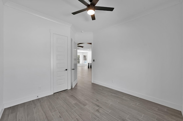 spare room with wood finished floors, crown molding, a ceiling fan, and baseboards