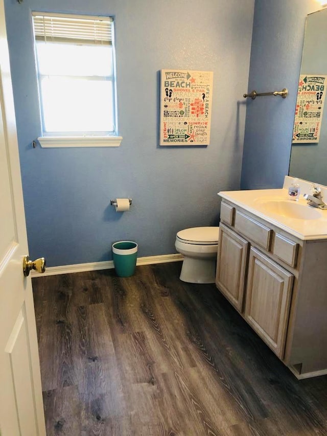 half bathroom featuring baseboards, toilet, wood finished floors, and vanity