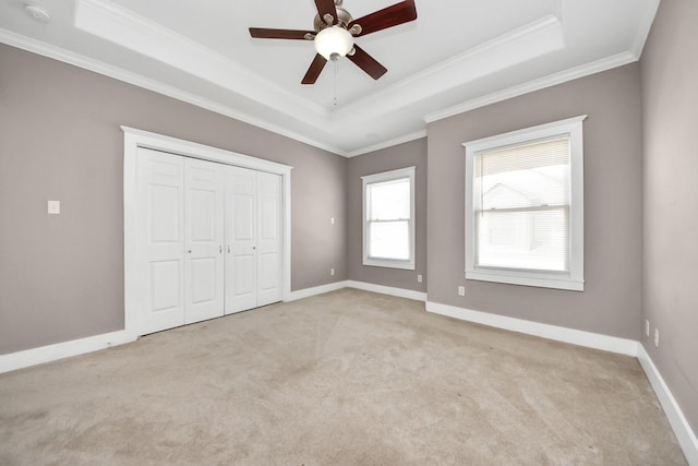 unfurnished bedroom featuring a tray ceiling, baseboards, light colored carpet, and crown molding