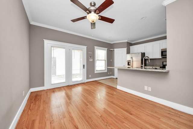 unfurnished living room with a sink, baseboards, ceiling fan, and crown molding