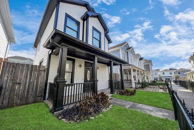 view of front of house featuring a front lawn, fence, covered porch, and a residential view