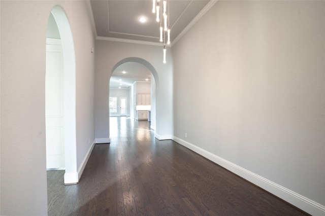 hallway with arched walkways, dark wood-style floors, crown molding, and baseboards