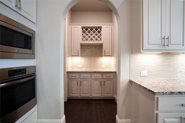 kitchen with dark wood-type flooring, arched walkways, appliances with stainless steel finishes, decorative backsplash, and baseboards