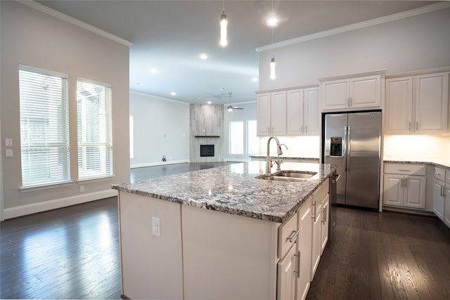 kitchen with light stone counters, dark wood-style floors, stainless steel fridge with ice dispenser, ornamental molding, and a sink